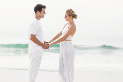 Romantic couple looking at each other and holding hands on the beach