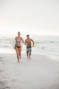 Couple with surfboard running on the beach on a sunny day