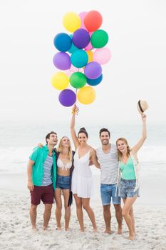 Group of happy friends standing on the beach with multicolored balloons