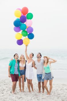 Group of happy friends standing on the beach with multicolored balloons