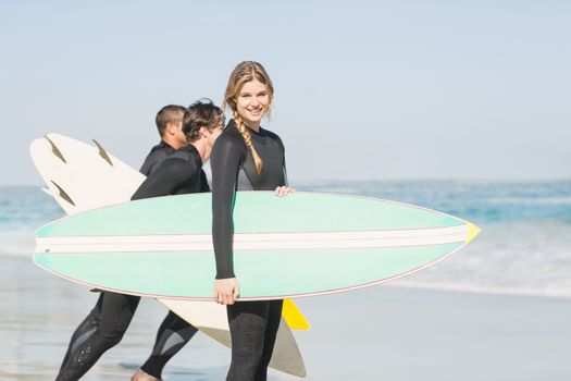 Portrait of surfer woman with surfboard standing on the beach and others surfer in background