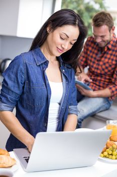 Couple using laptop and digital tablet in the kitchen during breakfast