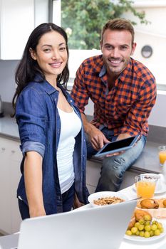 Portrait of couple using laptop and digital tablet in the kitchen