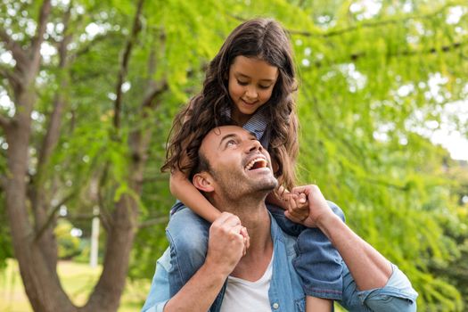 Father carrying daughter on his shoulders and smiling outdoors