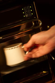 Hand with motion blur taking a coffee cup out of the espresso machine