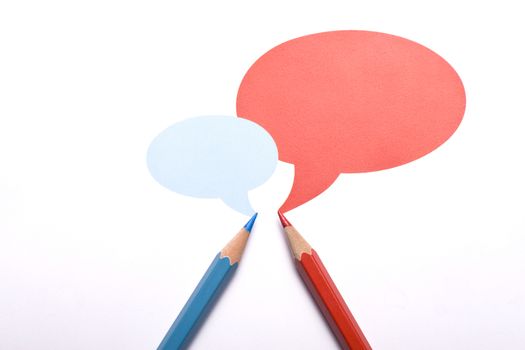 Horizontal top view of a red and a blue pencil with speech bubbles of different sizes above them isolated on white background. 
