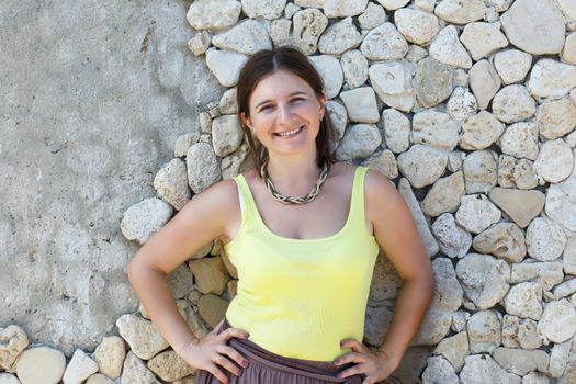 Smiling young woman in green t-shirt posing against the backdrop of an old stone wall.