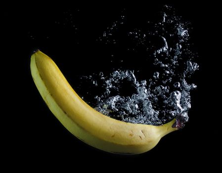 Banana dropped into water on black background. Air bubbles in water.