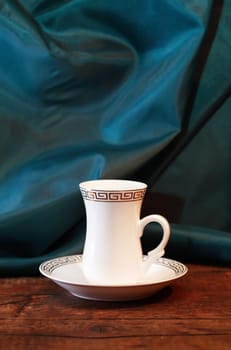 Stylish white coffee cup with saucer on dark cloth background