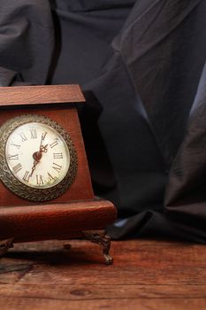 Still life with old vintage table clock on wooden board against dark cloth