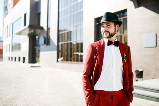 Stylish man in a hat in a red suit, with a beard and mustache, on the street.