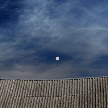 tiled top of the roof, cloudy blue sky and the moon at night 