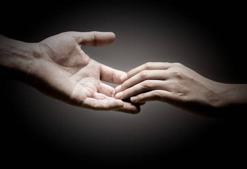 two hands are touching each other over black background, concept of solidarity or empathy.