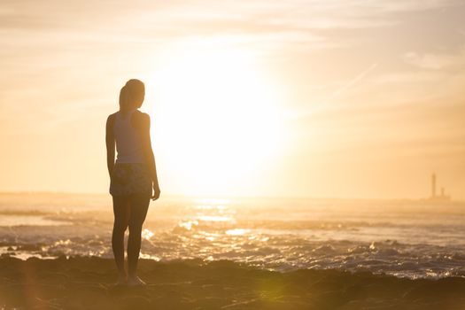 Silhouette of meditative, sensual blonde woman watching sunset at the beach.