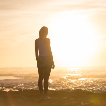 Silhouette of meditative, sensual blonde woman watching sunset at the beach.