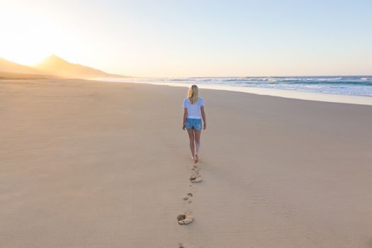 Woman walking on sandy beach in sunset leaving footprints in the sand. Beach, travel, concept. Copy space.