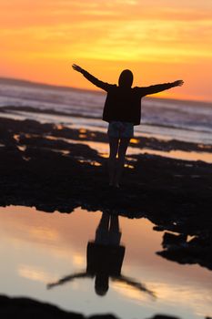 Silhouette of free woman enjoying freedom feeling happy at beach at sunset. Serene relaxing woman in pure happiness and elated enjoyment with arms raised outstretched up. 