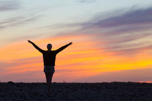 Silhouette of free woman enjoying freedom feeling happy at sunset. Serene relaxing woman in pure happiness and elated enjoyment with arms raised outstretched up. 