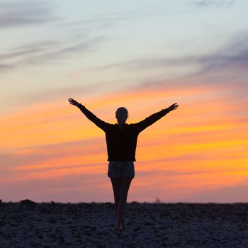 Silhouette of free woman enjoying freedom feeling happy at sunset. Serene relaxing woman in pure happiness and elated enjoyment with arms raised outstretched up. 