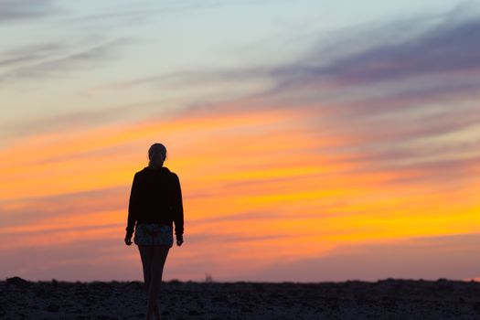 Silhouette of meditative, sensual blonde woman watching sunset at the beach.