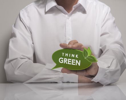 Image of a man hand holding speech balloon with the textthink green, white shirt. Concept for ecology or environment preservation.