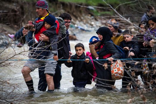 GREECE, Idomeni: Migrants and refugee cross a surging river on their way to Macedonia from a makeshift camp at the Greek-Macedonian border, near the Greek village of Idomeni on March 14, 2016, where thousands of them are stranded by the Balkan border blockade. More than 14,000 people are stuck on the Greek side of the border in an overcrowded camp at Idomeni after the main migrant route to western Europe through the Balkans was effectively shut down last week.