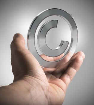 Man hand holding copyright symbol over grey background, concept image for illustration  of intellectual property.