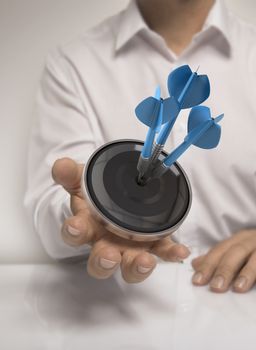 Man hand holding a target with three darts hitting the center, blue and beige tones, concept image for illustration of marketing or business solutions