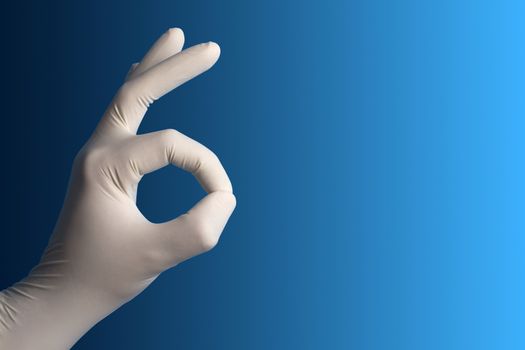 Hand with a white surgical glove showing the ok sign against a blue background