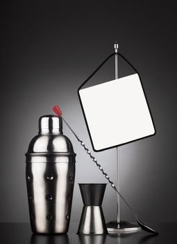 Cocktail set of tools including shaker and spoon next to a table stander with display area for offers or headline