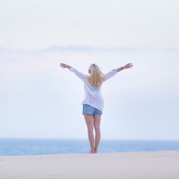 Relaxed woman enjoying freedom feeling happy at beach in the morning. Serene relaxing woman in pure happiness and elated enjoyment with arms raised outstretched up. 