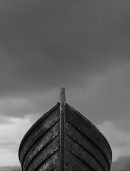 Vertical front view of an old fishing wood boat with rusted nails with dramatic grey storm clouds in the background