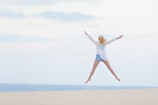 Relaxed woman enjoying freedom, feeling happy. Serene relaxing woman in pure happiness and elated enjoyment, jumping with arms outstretched up. Copy space for text.