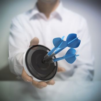 Man holding on black target with three blue darts hitting the center. Concept image for illustration of Marketing and advertising success or self confidence.
