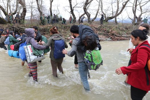 GREECE, Idomeni: Migrants and refugee cross a surging river on their way to Macedonia from a makeshift camp at the Greek-Macedonian border, near the Greek village of Idomeni on March 14, 2016, where thousands of them are stranded by the Balkan border blockade. More than 14,000 people are stuck on the Greek side of the border in an overcrowded camp at Idomeni after the main migrant route to western Europe through the Balkans was effectively shut down last week.