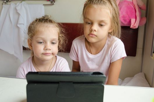 Two girls sisters sitting in the train watching cartoon Tablet PC