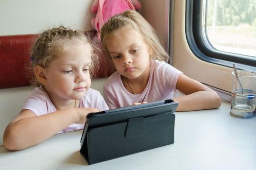 Two girls sisters sitting in the train watching a cartoon in the plate