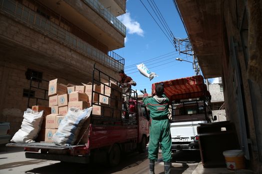 SYRIA, Saqba: A man carries a sack of wheat as Syrian Red Crescent staff survey the delivery of humanitarian aid at a warehouse in Saqba, in the rebel-held Eastern Ghouta area, southern Syria, on the outskirts of the capital Damascus on March 15, 2016 during an operation in cooperation with the UN to deliver aid to thousands of besieged Syrians. UN aid convoys head to two Syrian towns besieged by government forces to deliver life-saving food and medicine to some 30,000 people, a UN spokesman said. 