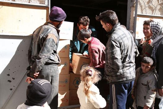 SYRIA, Saqba: A child carries a food pack as Syrian Red Crescent staff survey the delivery of humanitarian aid at a warehouse in Saqba, in the rebel-held Eastern Ghouta area, southern Syria, on the outskirts of the capital Damascus on March 15, 2016 during an operation in cooperation with the UN to deliver aid to thousands of besieged Syrians. UN aid convoys head to two Syrian towns besieged by government forces to deliver life-saving food and medicine to some 30,000 people, a UN spokesman said. 