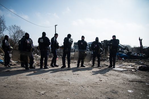 FRANCE, Calais: French anti-riot policemen stand guard during the dismantling of the southern part of the so-called 'Jungle' migrant camp in Calais, northern France, on March 14, 2016.Thousands of migrants have been living in the Jungle and other smaller camps along the northern coast, desperate to reach Britain where many have family or community ties and see better hopes of gaining employment or education. 