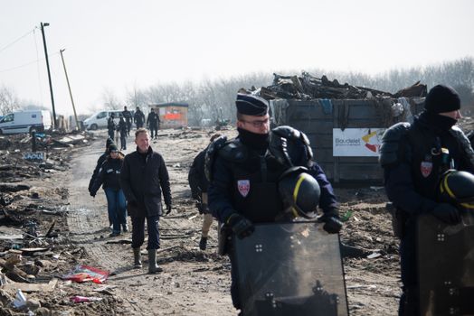 FRANCE, Calais: French anti-riot policemen stand guard during the dismantling of the southern part of the so-called 'Jungle' migrant camp in Calais, northern France, on March 14, 2016.Thousands of migrants have been living in the Jungle and other smaller camps along the northern coast, desperate to reach Britain where many have family or community ties and see better hopes of gaining employment or education. 