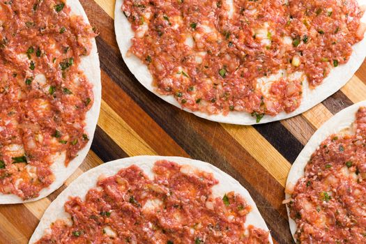 Food background of prepared uncooked Turkish lahmacun with a round dough base topped with minced savory meat and vegetables with herbs, close up overhead view