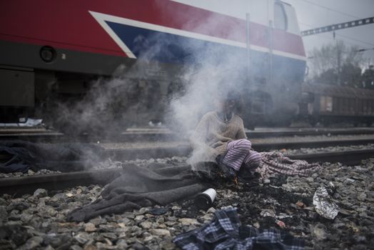 GREECE, Idomeni: A girl warms along the railway tracks next to tents at the Idomeni refugee camp on the Greek Macedonia border on March 15, 2016 in Idomeni, Greece. Yesterday, an attempt by some of the residents of the camp to cross the border to Macedonia was thwarted by Macedonian security forces who returned the migrants to Greece. The decision by Macedonia to close its border to migrants last week has left thousands of people stranded at the Greek transit camp. The closure, following the lead taken by neighbouring countries, has effectively sealed the so-called western Balkan route, the main migration route which has been used by hundreds of thousands of migrants to reach countries in western Europe, such as Germany. Humanitarian workers have described the conditions at the camp as desperate, which has been made much worse by recent spells of heavy rain.
