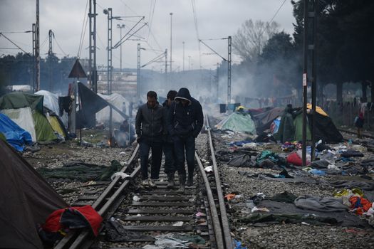 GREECE, Idomeni: Men walk along the railway tracks next to tents at the Idomeni refugee camp on the Greek Macedonia border on March 15, 2016 in Idomeni, Greece. Yesterday, an attempt by some of the residents of the camp to cross the border to Macedonia was thwarted by Macedonian security forces who returned the migrants to Greece. The decision by Macedonia to close its border to migrants last week has left thousands of people stranded at the Greek transit camp. The closure, following the lead taken by neighbouring countries, has effectively sealed the so-called western Balkan route, the main migration route which has been used by hundreds of thousands of migrants to reach countries in western Europe, such as Germany. Humanitarian workers have described the conditions at the camp as desperate, which has been made much worse by recent spells of heavy rain.