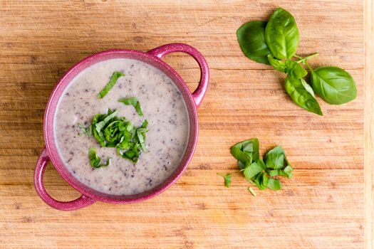 Delicious homemade cream of mushroom soup with minced fresh mushrooms garnished with chopped basil, overhead view in a ceramic bowl on a bamboo cutting board