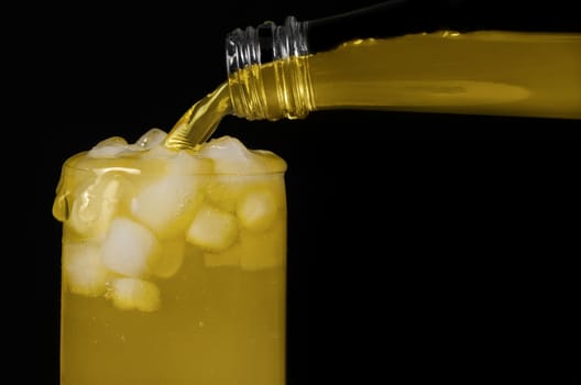 The lemonade poured over the edge ,from a bottle into a glass with ice. Black background.