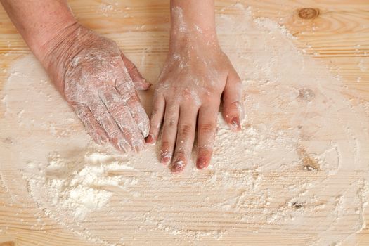 hands of the grandmother and hand of the granddaughter lie on a wooden board with flour