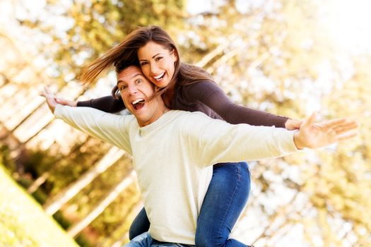 Beautiful young couple enjoying a piggyback in the park. Looking at camera and smiling.