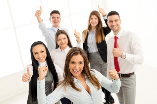 Successful young businesswoman standing proudly with her young business team. They showing thumbs up and looking at camera.