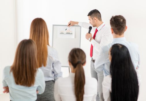 Businesspeople having meeting in a office. Young businessman standing  in front of flip chart and having presentation.